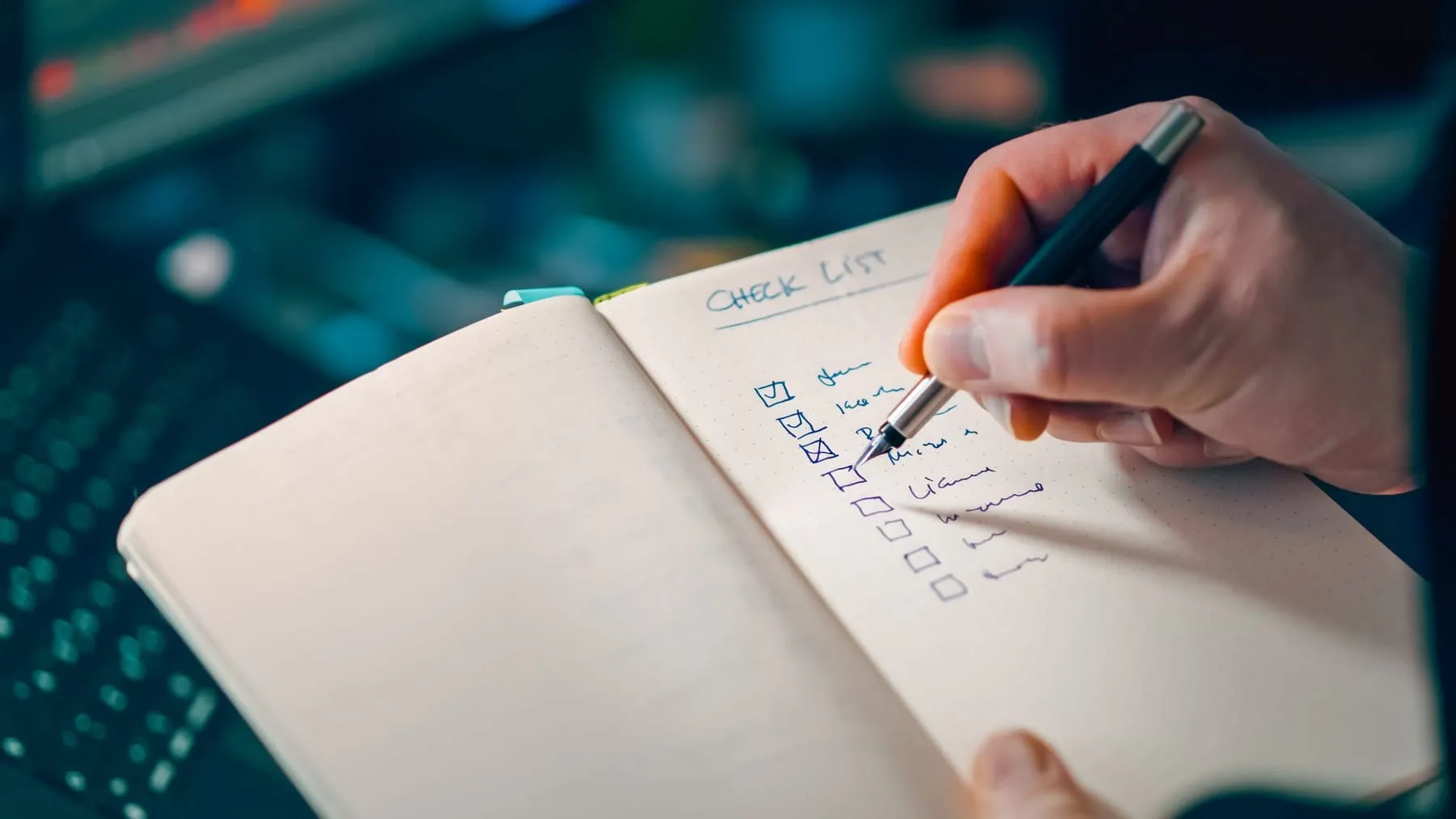 A hand ticking items off a handwritten checklist in a notebook