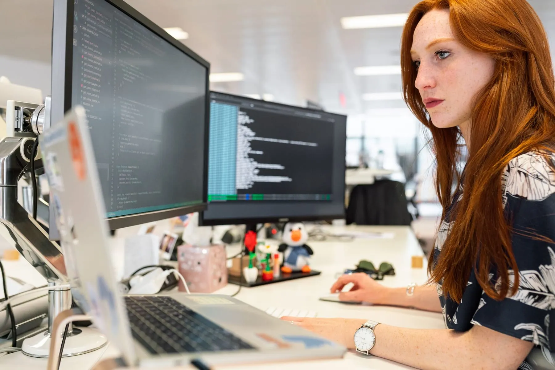 A software engineer writing code across two monitors in an open office